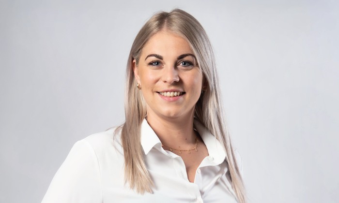 Die Grafik zeigt eine Frau mit langen, glatten Haaren in einer weißen Bluse vor einem neutralen Hintergrund. Ihr Gesicht ist verpixelt, wodurch ihre Identität anonym bleibt.