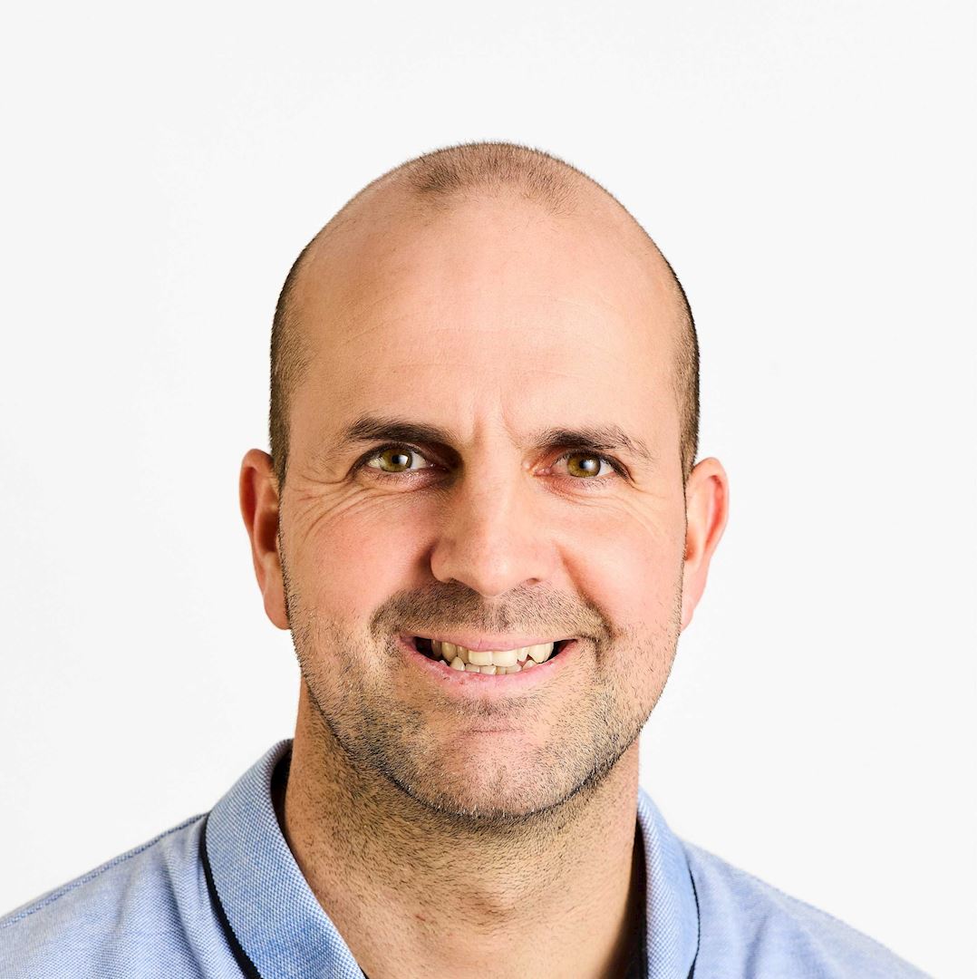 Ein Mann in einem blauen Hemd, der vor einem weißen Hintergrund fotografiert wurde; sein Gesicht ist aus Datenschutzgründen verpixelt.